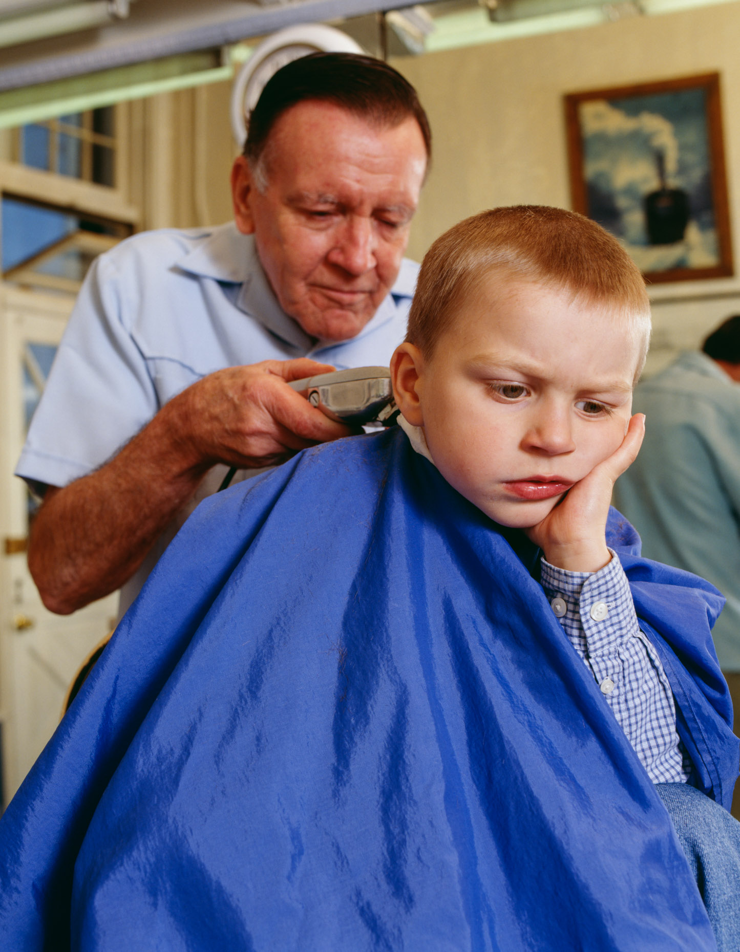 Boy (4-5 years old) having hair cut by male barber.