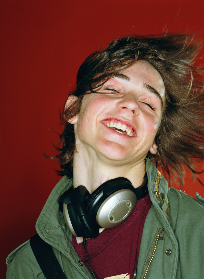 Teenage boy (14-16) tossing head back, smiling, headphones around neck